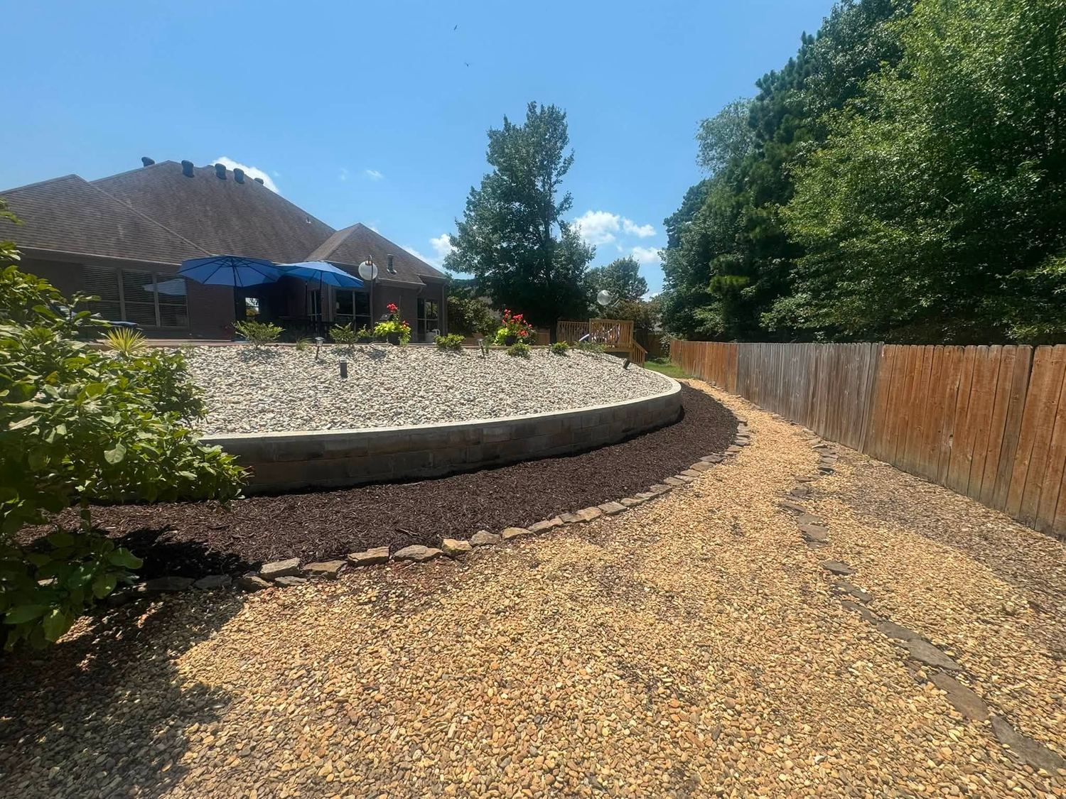 The same slope cleared, with a clean stone wall, gravel, and mulched beds