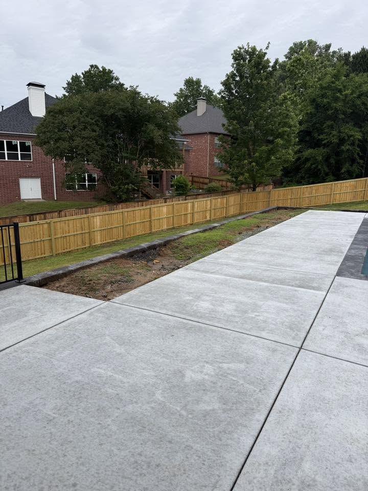 Bare dirt planting strip beside a new concrete patio and fence
