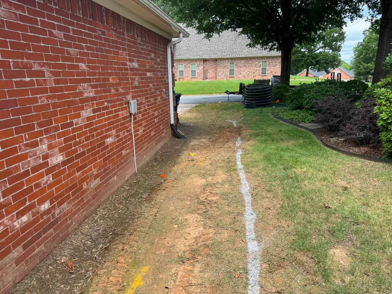Bare dirt marked with layout paint along the side of a brick home