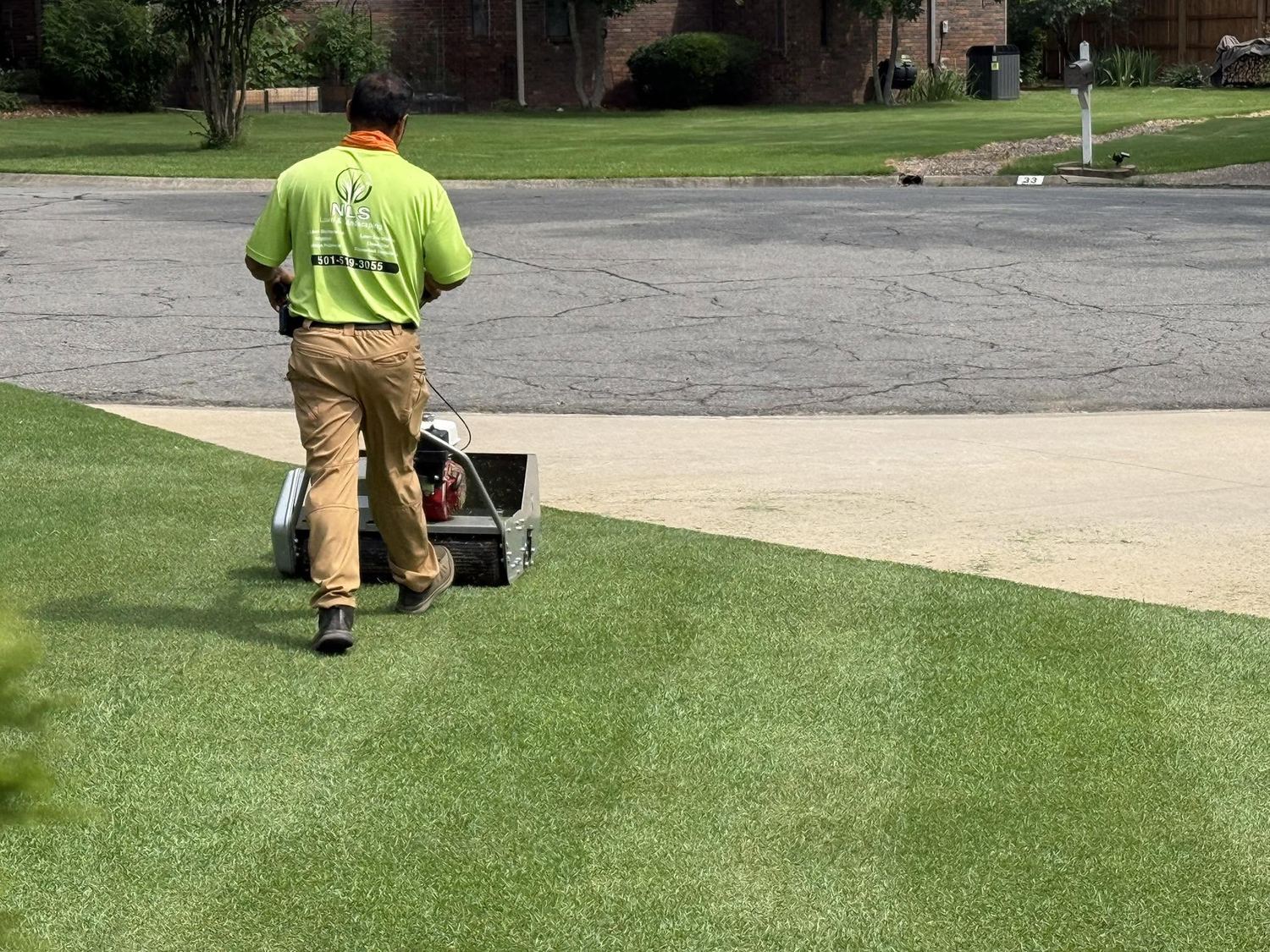 NLS team member mowing a striped lawn in a company shirt