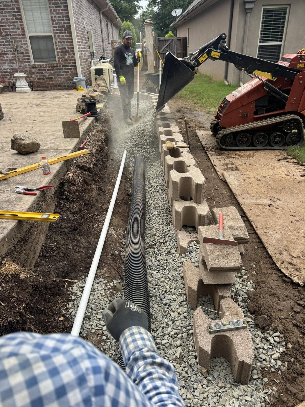 Retaining wall blocks and gravel drainage bed being installed beside a home
