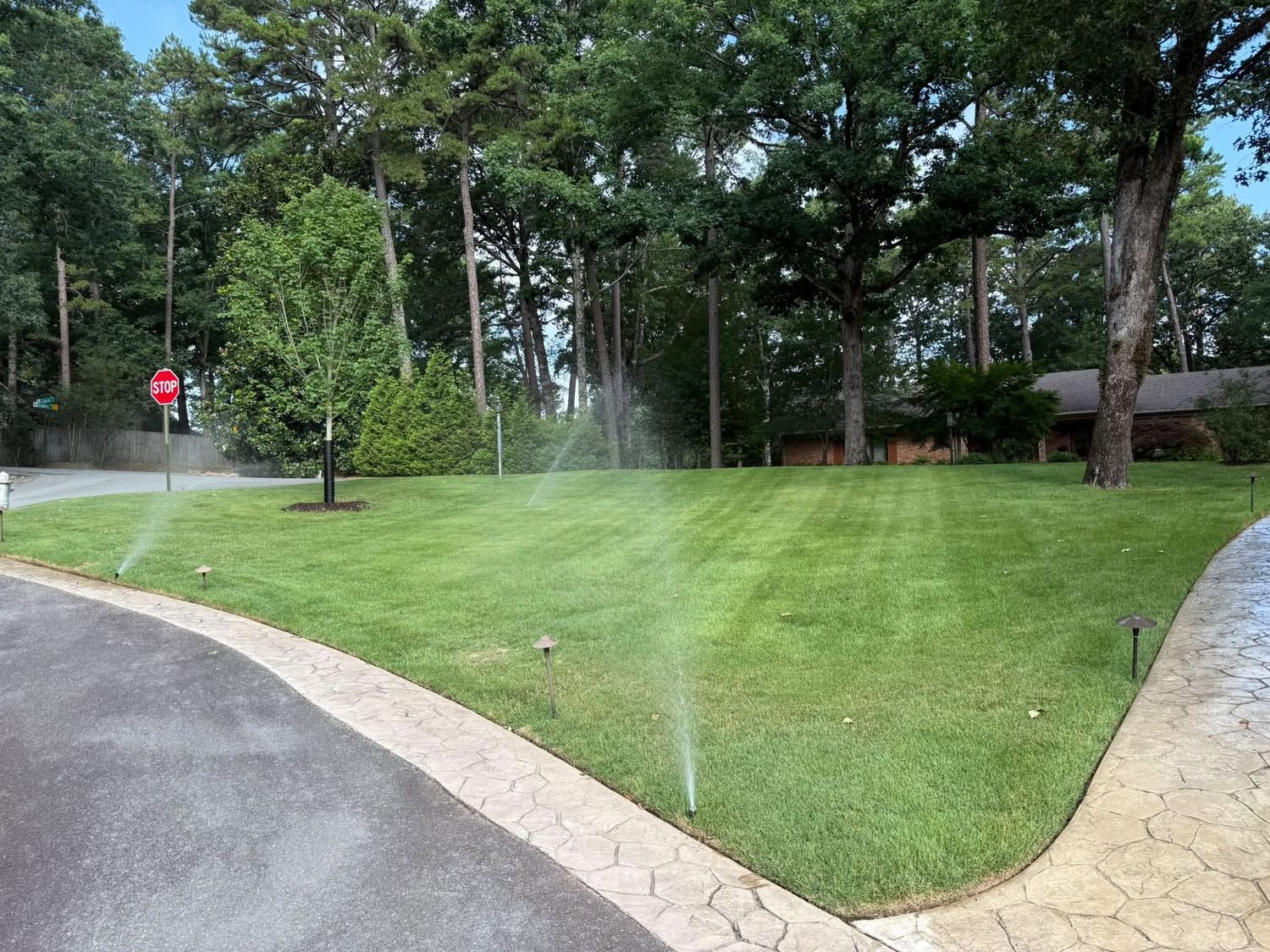 Irrigation sprinklers running across a lush striped lawn beside a stamped concrete drive